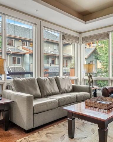 Bright living room with gray sofa, leather armchair, wood coffee table, and floor-to-ceiling windows