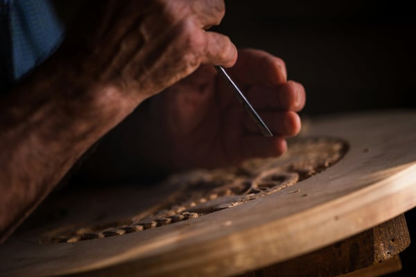 Hands carefully carving intricate wood detail — excellence and craftsmanship