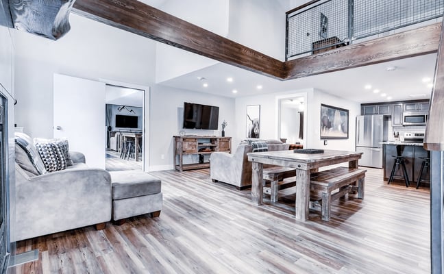 Open-plan living space with wood beams, pool table, gray sofa, and kitchen visible in background