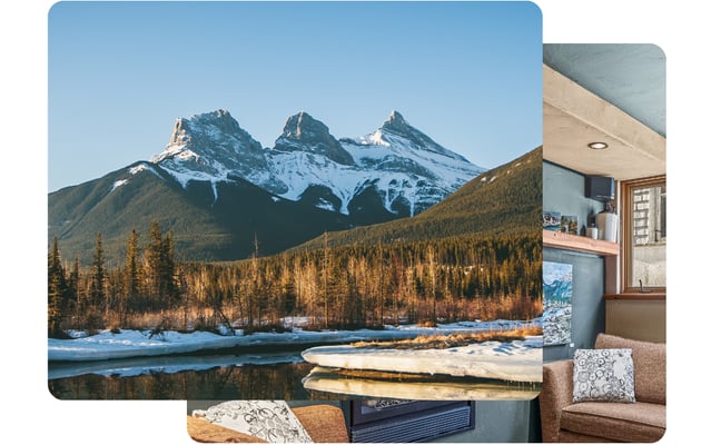 Mountain view with snow-capped peaks and forested valley visible through cabin window, interior with fireplace and seating in foreground